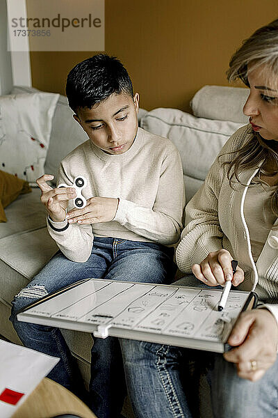 Mutter unterrichtet autistischen Jungen  während er auf dem Sofa im Wohnzimmer sitzt