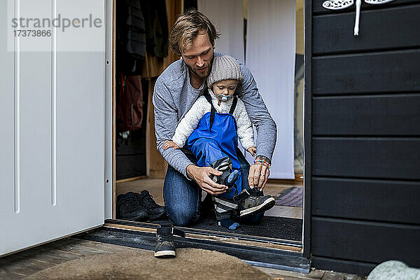 Mittlerer Erwachsener  der seinem Sohn beim Anziehen der Schuhe an der Tür hilft