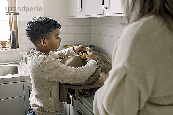 Autistischer Junge  der zu Hause bei seiner Mutter eine Banane in die Tasche steckt