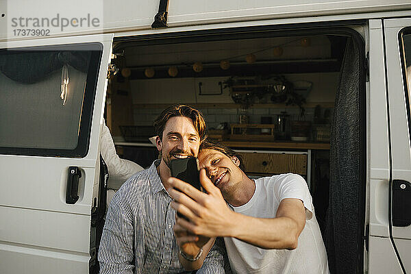 Homosexuelles Paar  das ein Selfie mit seinem Smartphone macht  während es an der Tür eines Wohnmobils sitzt