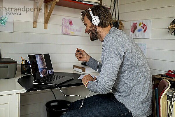 Lächelnder Mann im Gespräch mit seiner Freundin per Videoanruf über einen Laptop zu Hause