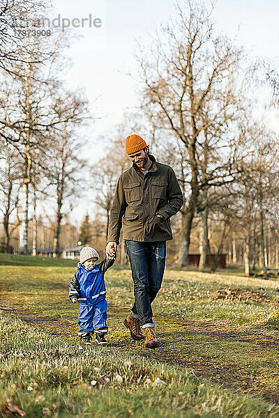 Vater und Sohn halten sich an den Händen  während sie gemeinsam im Park spazieren gehen