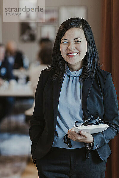 Porträt einer glücklichen Unternehmerin mit Tagebuch in einem Firmenbüro