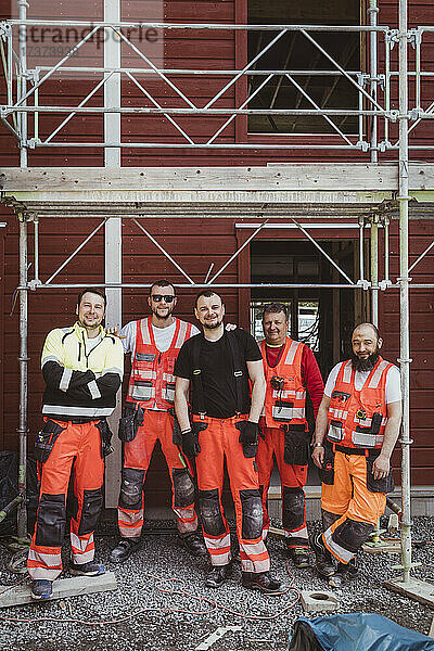Männliche Bauarbeiter stehen auf der Baustelle in voller Länge zusammen