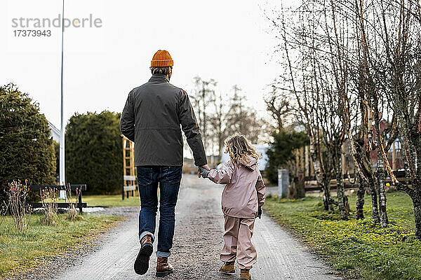 Rückansicht in voller Länge  Vater und Tochter halten sich an den Händen  während sie auf der Straße gehen