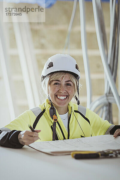 Porträt einer glücklichen Bauunternehmerin mit Grundriss auf einer Baustelle