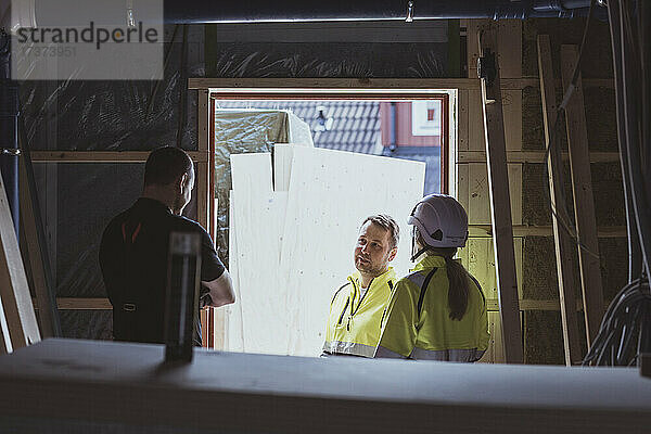 Männlicher Bauarbeiter im Gespräch mit einem Kollegen und einer Bauunternehmerin auf der Baustelle