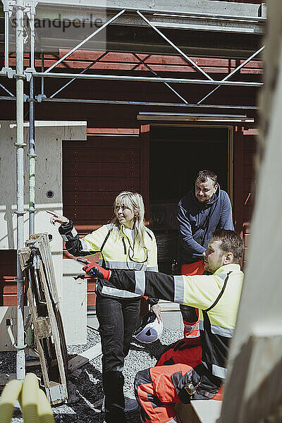 Weiblicher Bauunternehmer mit männlichem Kollegen  der an einem sonnigen Tag auf eine Baustelle zeigt