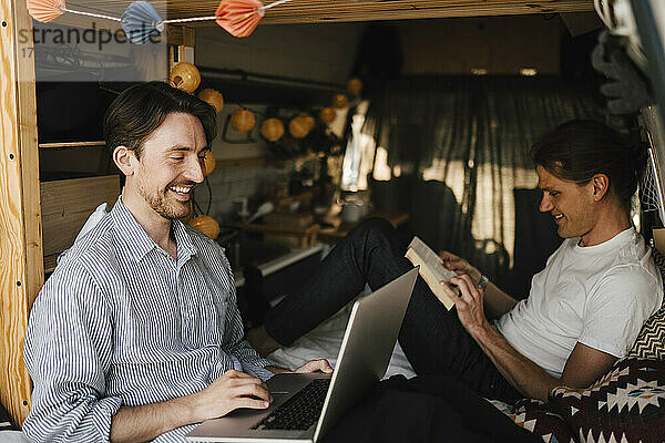 Lächelnder Mann mit Laptop bei seinem Freund im Campingbus