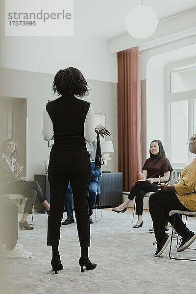Rückansicht einer Geschäftsfrau  die einen Vortrag vor einem männlichen und einem weiblichen Angestellten in einer Schulklasse hält