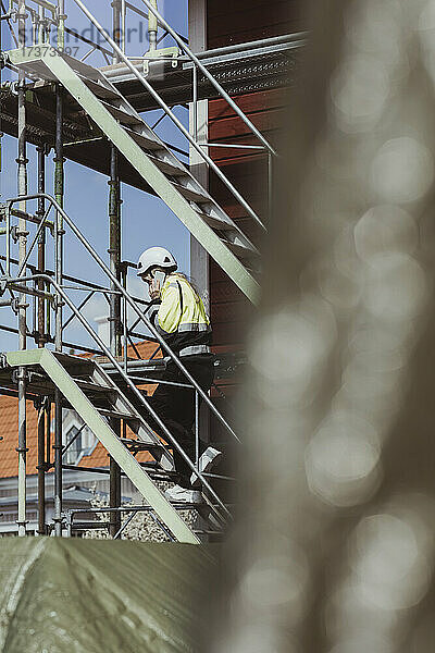 Bauunternehmerin in voller Länge  die mit ihrem Smartphone telefoniert  während sie auf der Baustelle die Stufen hinaufgeht