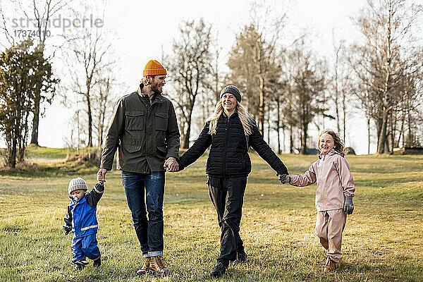 Fröhliche Familie in voller Länge  die sich beim gemeinsamen Spaziergang im Park an den Händen hält