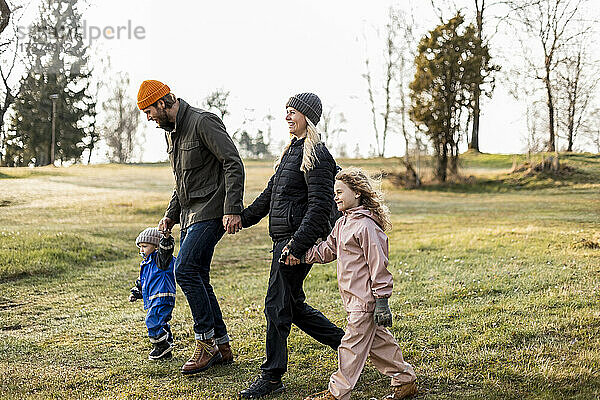 Glückliche Familie in voller Länge  die sich beim gemeinsamen Spaziergang im Park an den Händen hält