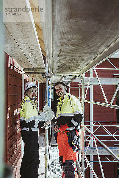 Eine lächelnde Bauarbeiterin diskutiert mit einem männlichen Kollegen  während sie zusammen auf einem Baugerüst stehen