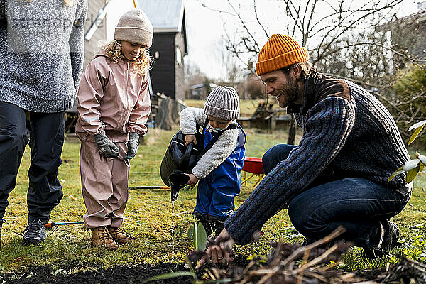 Mann führt Sohn mit Gießkanne durch Mädchen bei der Gartenarbeit im Hinterhof