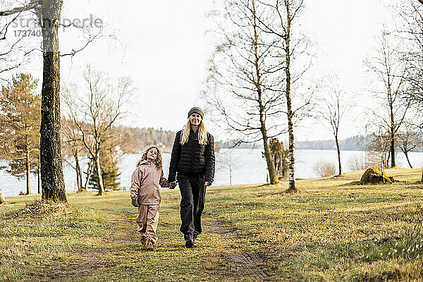 Frau in voller Länge mit Tochter spazieren gehend und Hände haltend im Park