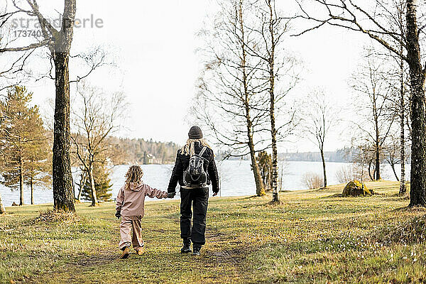 Rückansicht in voller Länge von Mutter und Tochter  die sich an den Händen halten  während sie zum See gehen