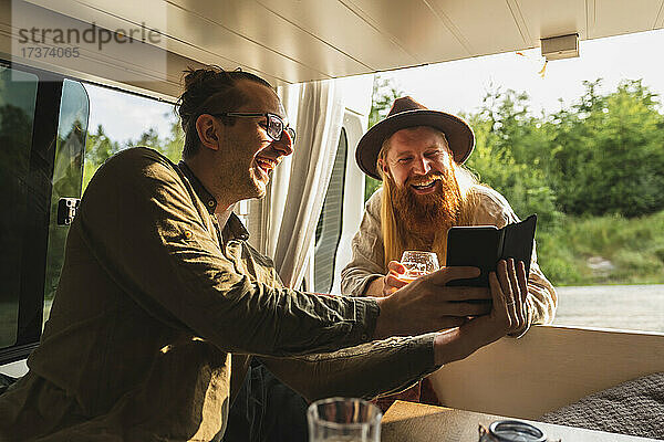 Glücklicher Mann  der sein Smartphone mit einem männlichen Freund im Campingbus teilt