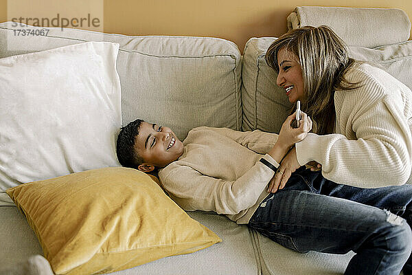 Lächelnde Mutter und Sohn spielen auf dem Sofa zu Hause