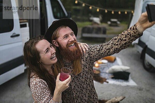 Glückliche männliche und weibliche Freunde  die beim Camping ein Selfie mit dem Smartphone machen