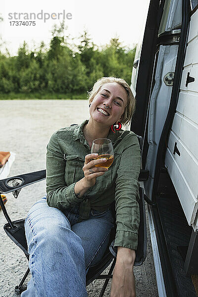 Porträt einer lächelnden Frau mit Bierglas bei einem Campingbus während einer Autoreise