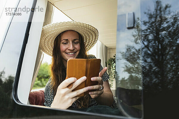 Lächelnde Frau  die ihr Smartphone benutzt  während sie im Wohnmobil sitzt