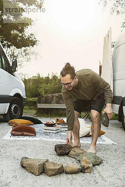 Junger Mann arrangiert Steine für ein Lagerfeuer im Urlaub