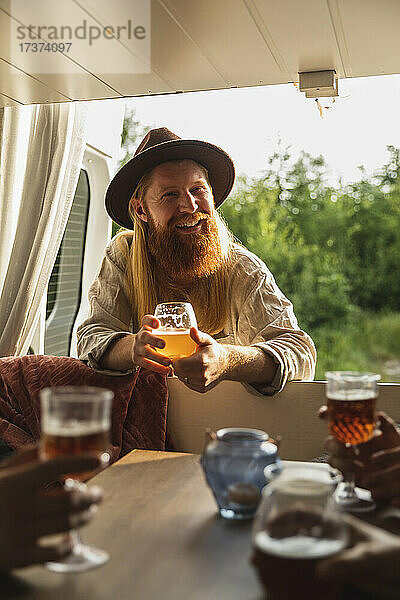 Bärtiger Mann mit Bierglas im Gespräch mit Freunden im Wohnmobil