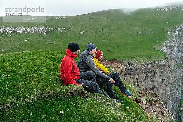 3 Wanderer sitzen mit Blick auf die Beinisforo Klippen  Sandvik  Suduroy  Faroer Inseln