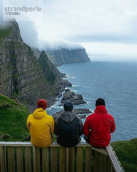 3 Wanderer sitzen auf Holzbank mit Blick auf die Beinisforo Klippen  Sandvik  Suduroy  Faroer Inseln