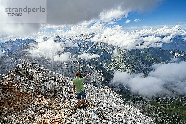 Wanderer deutet in die Ferne  am Gipfel der Partenkirchner Dreitorspitze  Blick ins Reintal auf wolkenverhangene Gipfel  hinten Zugspitzplatt und Zugspitze  Wettersteingebirge  Garmisch Partenkirchen  Bayern  Deutschland  Europa