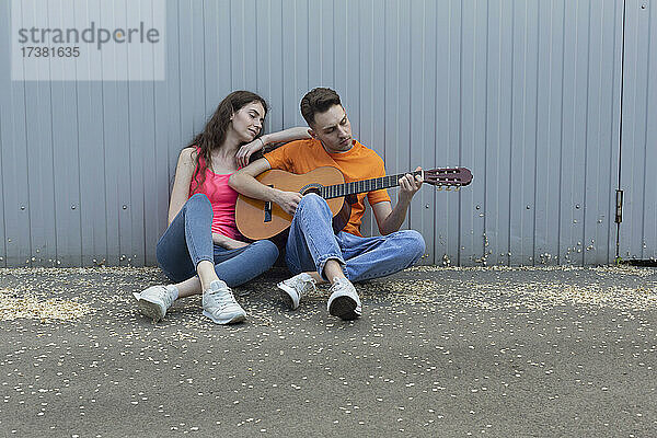 Junges Paar spielt Gitarre an der Wand