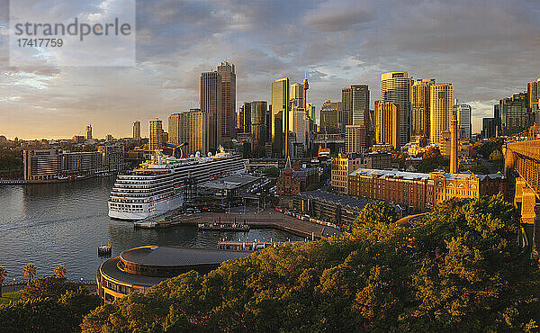 Kreuzfahrtschiff im Hafen von Sydney mit Wolkenkratzern im Hintergrund.