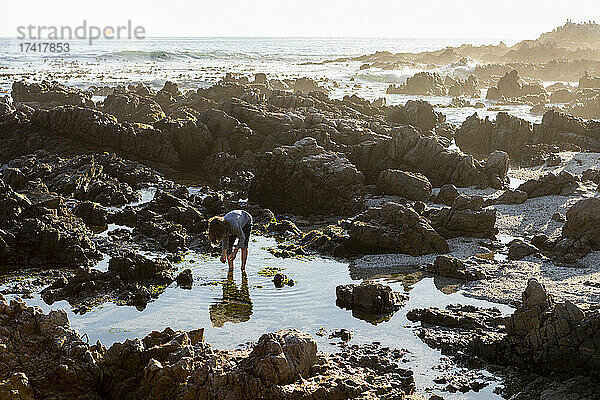 Junge erkundet einen Felsentümpel an der Küste bei Sonnenuntergang