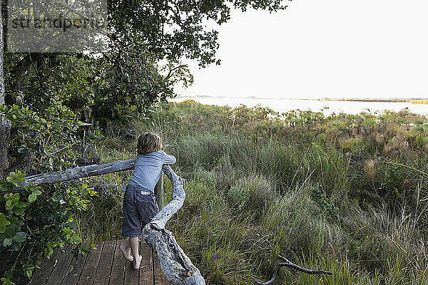 Ein kleiner Junge auf einem Steg  der aus einem Zelt im Okavango-Delta herausschaut