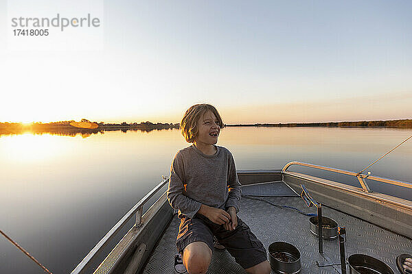 Ein Junge auf dem Deck eines kleinen Bootes im Okavango-Delta bei Sonnenuntergang  Botswana.