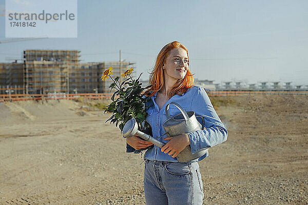 Frau trägt Topfpflanze und Gießkanne auf der Baustelle