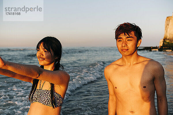 Männliche und weibliche Freunde schauen weg  während sie bei Sonnenuntergang am Strand stehen