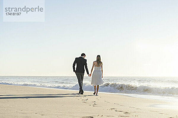 Frischvermähltes Paar hält Händchen beim Spaziergang am Strand