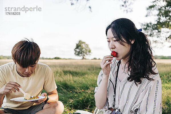 Frau isst Erdbeeren  während sie beim Picknick mit Mann im Park sitzt