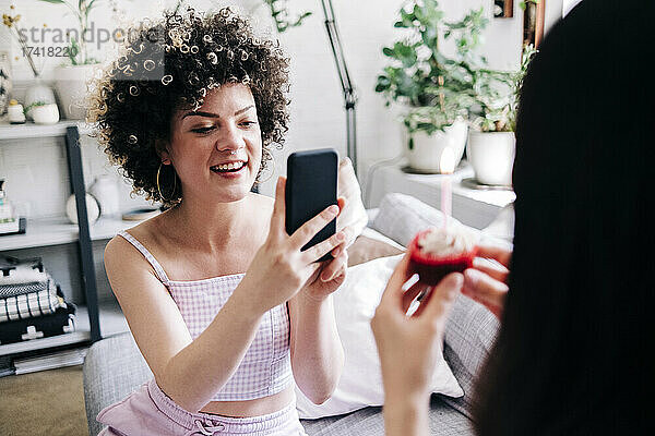 Lächelnde Frau fotografiert Freundin zu Hause per Smartphone