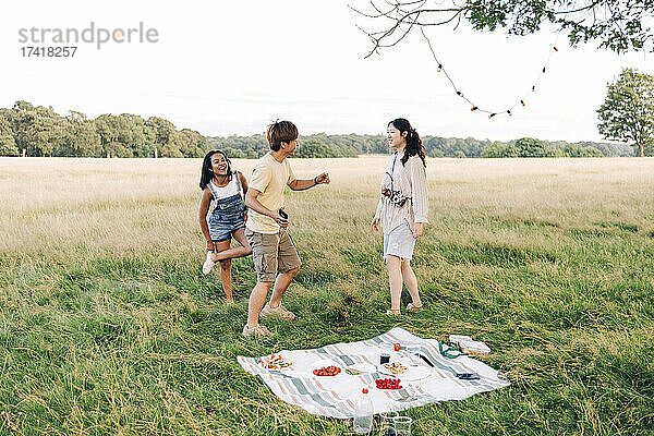 Fröhliche Freunde tanzen beim Picknick auf der Wiese