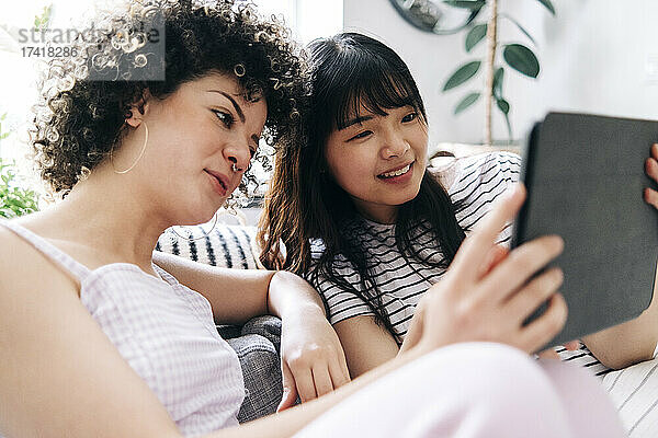 Lächelnde Frau nutzt digitales Tablet mit Freundin zu Hause