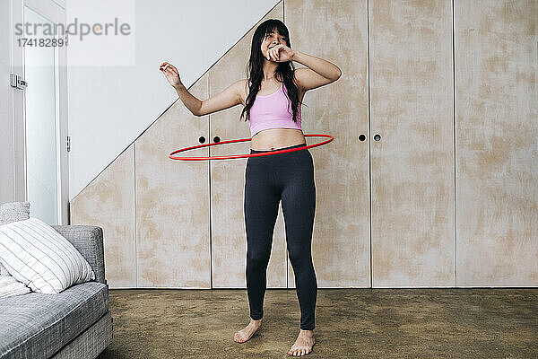 Frau dreht Plastikreifen  während sie zu Hause trainiert