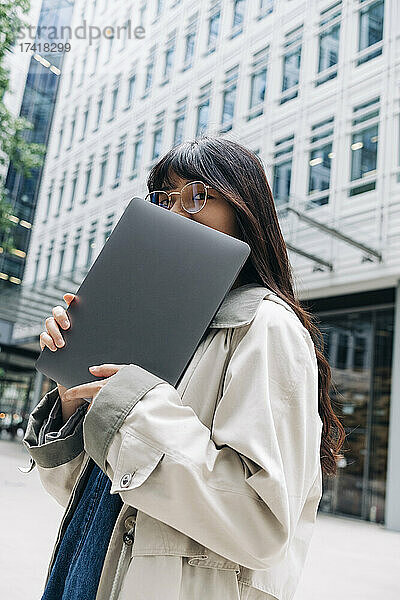 Frau mit Brille bedeckt Gesicht mit Laptop in der Stadt