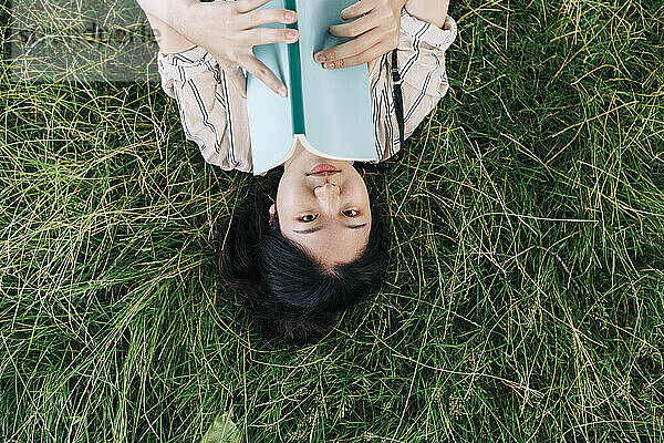 Frau hält Buch  während sie auf Gras liegt