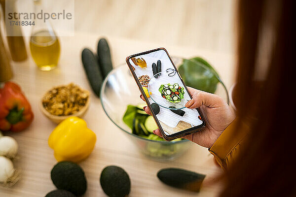 Frau fotografiert Salatschüssel mit Handy am Tisch