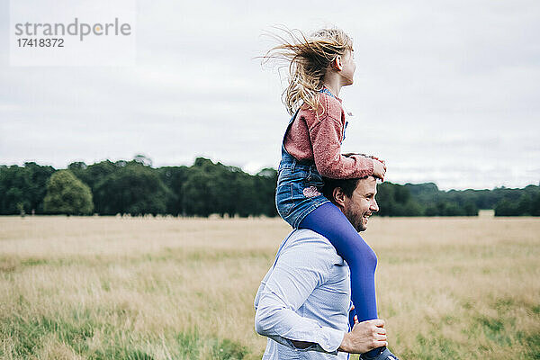 Glücklicher Vater trägt Tochter auf Schultern auf der Wiese