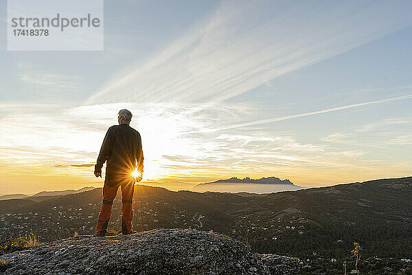 Mann steht auf einer Klippe und blickt auf den Berg