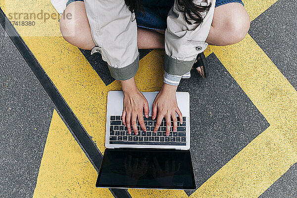 Junge Frau benutzt Laptop  während sie auf der Straße sitzt